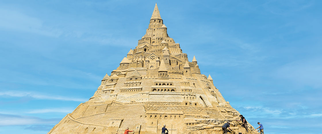 a giant, elaborate sandcastle with a few people working at the base of it